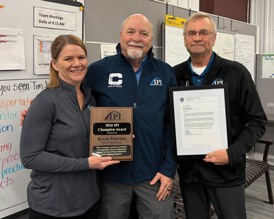 Kevin Peterson standing in between Sales & Marketing Manager Ann Baughman (Left) and IPI Director Bob Fairfax (Right) while wearing his IPI Change Champion Jacket. Ann is holding Kevin's Champion Award plaque and Bob is holding his letter from the Governor.